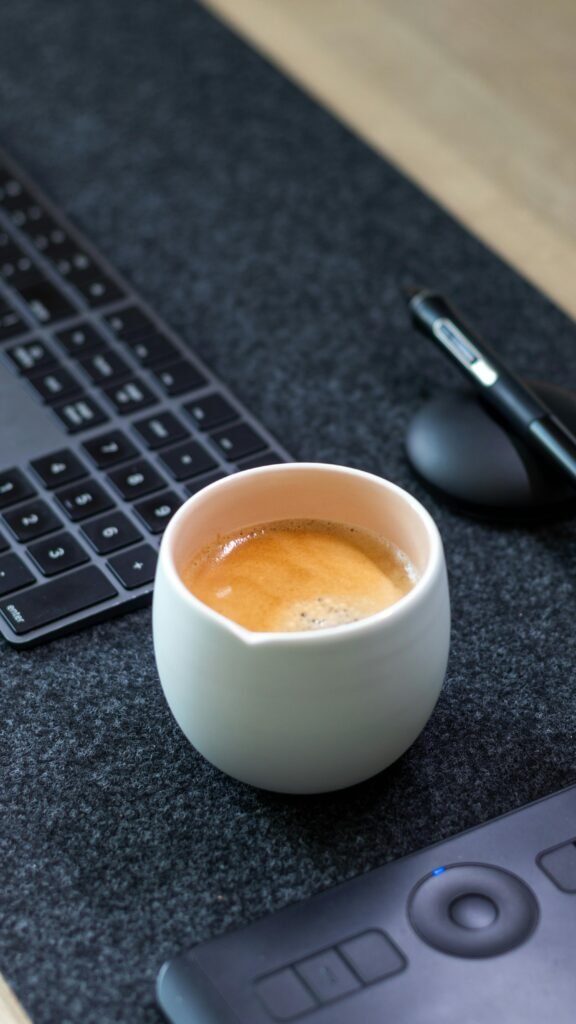 A cozy office desk setup featuring a cup of cappuccino, keyboard, and stylus for productivity.